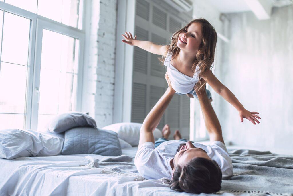 Eine Person hält ein kleines Kind in die Luft auf einem Bett