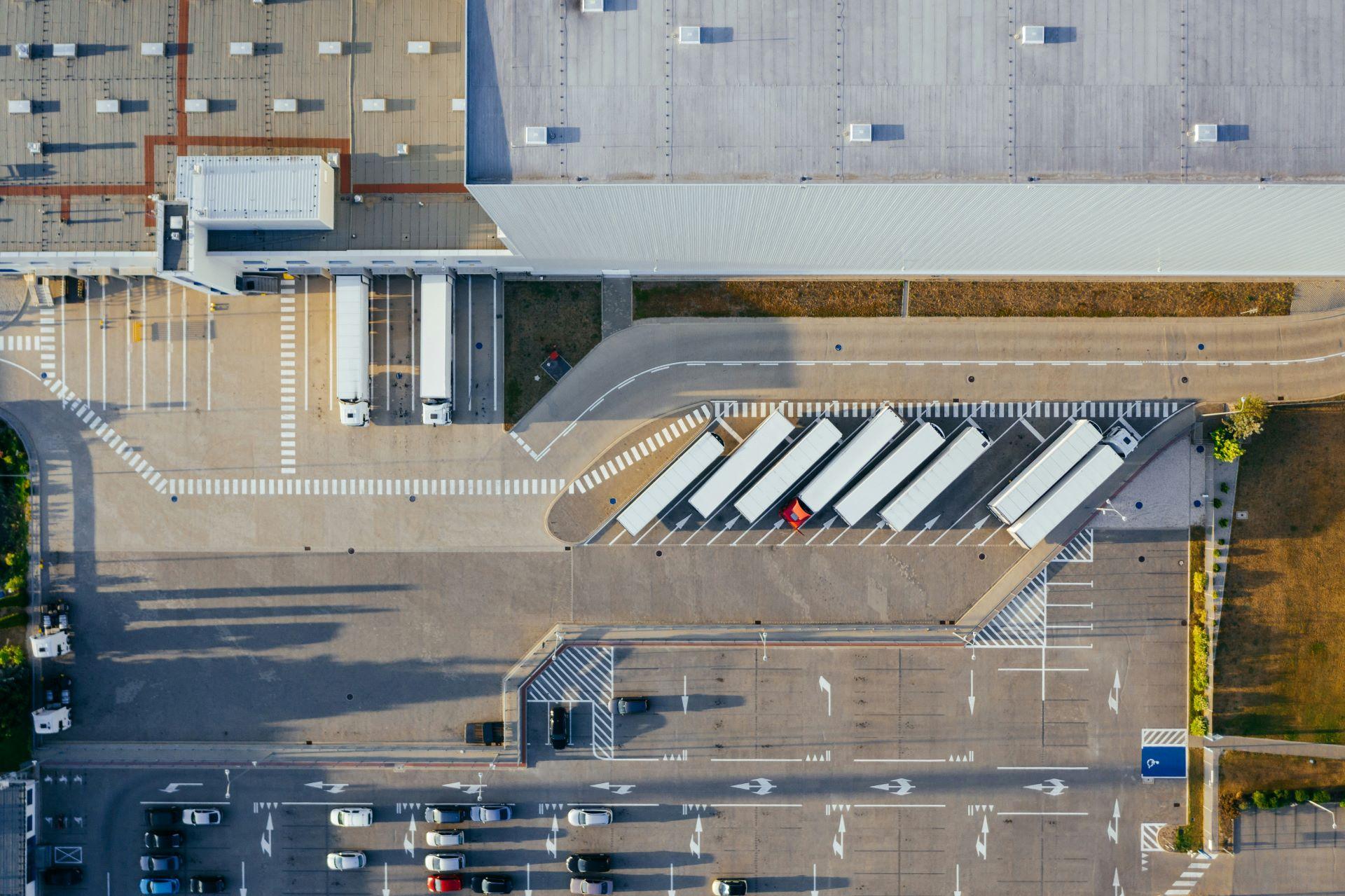 Luftaufnahme eines modernen Logistikzentrums mit parkenden LKWs in der Ladezone.