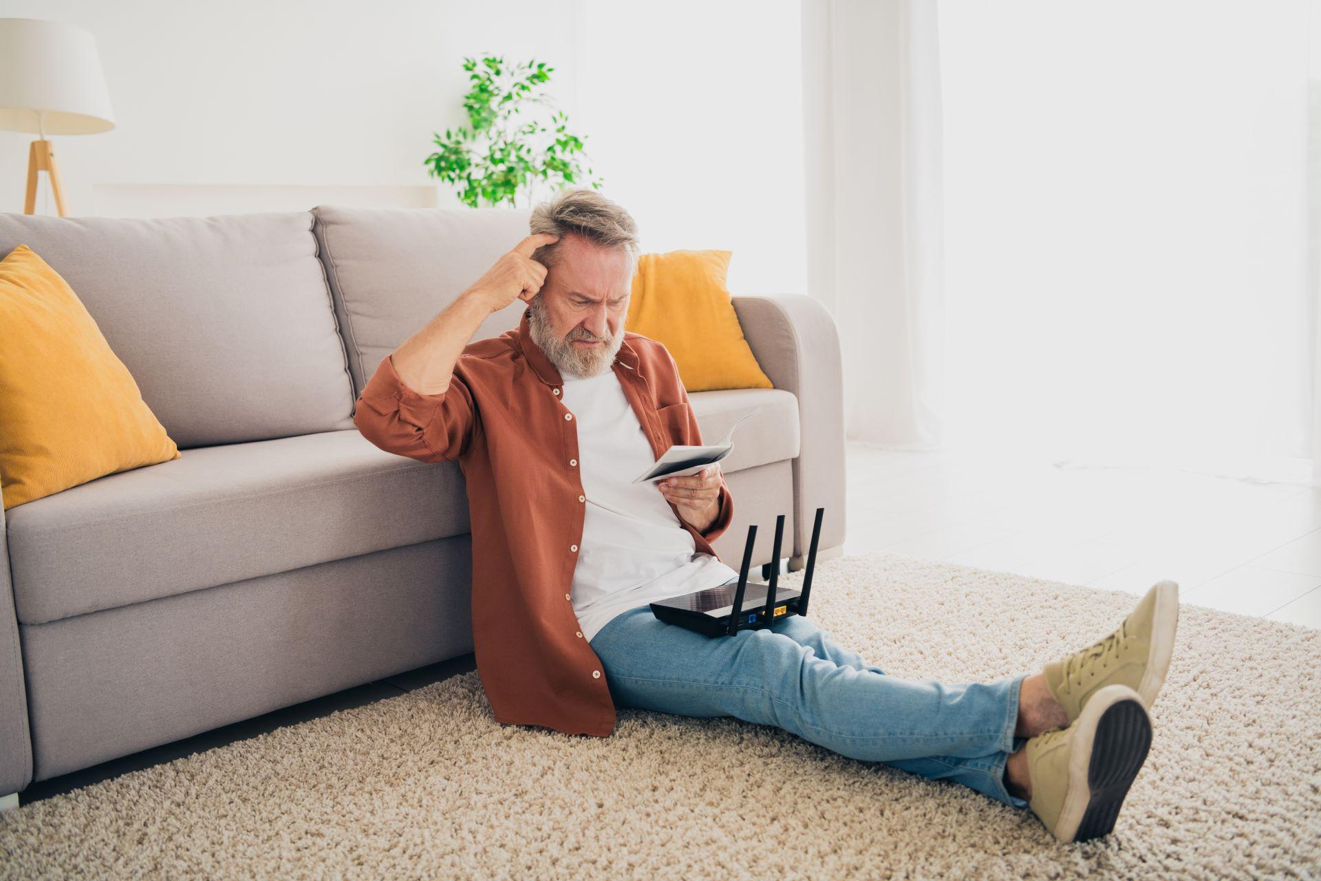 Älterer Mann prüft Router und Anleitungen, steht für technische Wartungsroutinen im Alltag.