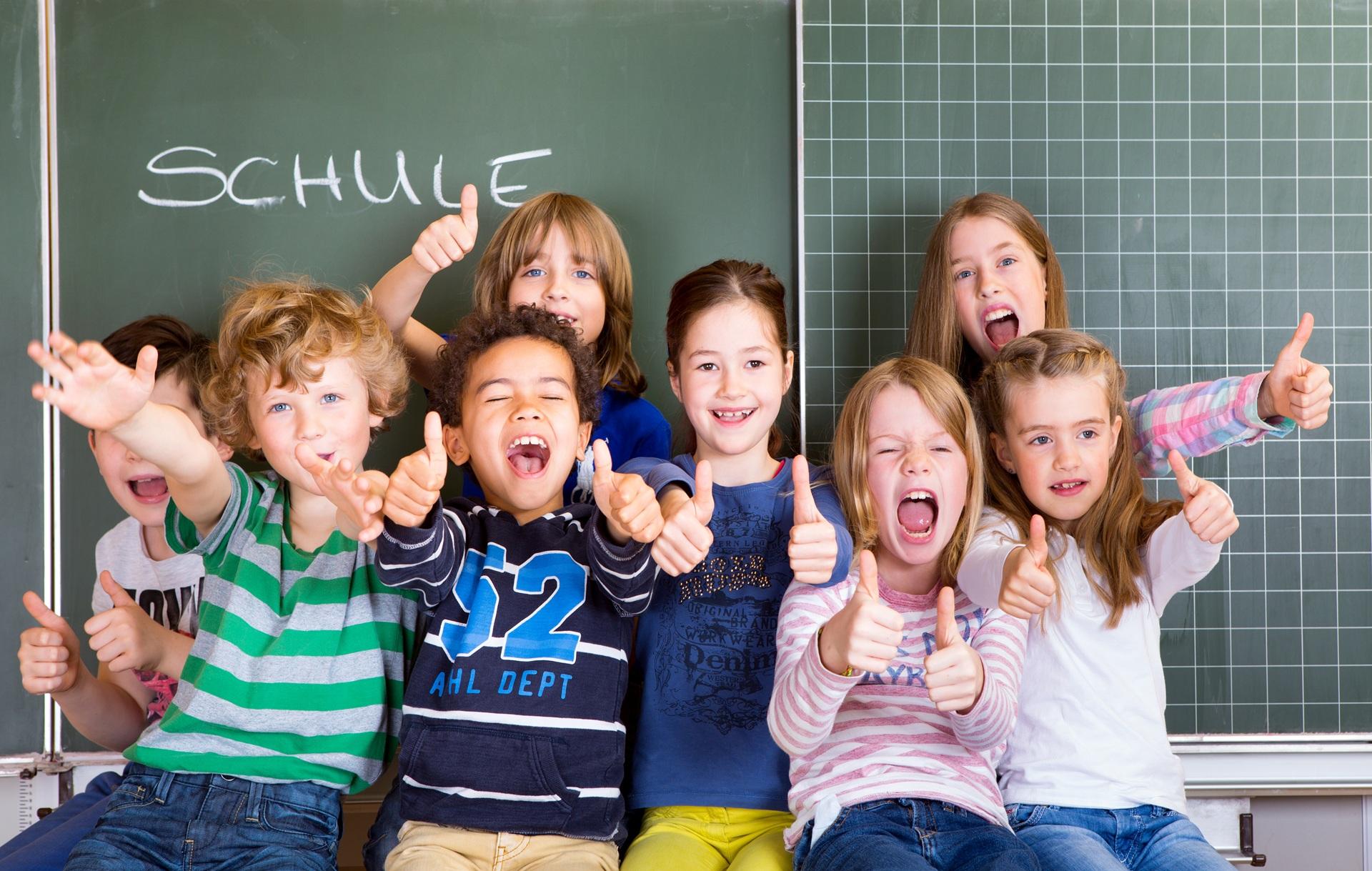 Fröhliche Kindergruppe zeigt Daumen hoch vor Tafel | Klassenfahrt München