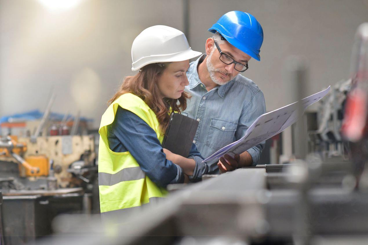 Ingenieurin und Ingenieur mit Bauplan besprechen die Integration einer Industrie Begleitheizung in eine Produktionsanlage