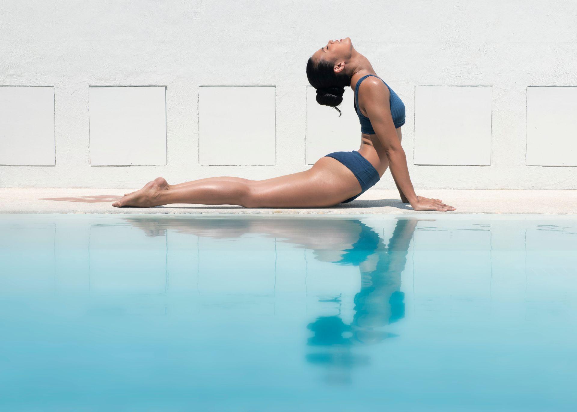 Frau macht Yoga Uebung am Poolrand, reflektiert im Wasser, Symbol fuer Ruhe und Gleichgewicht